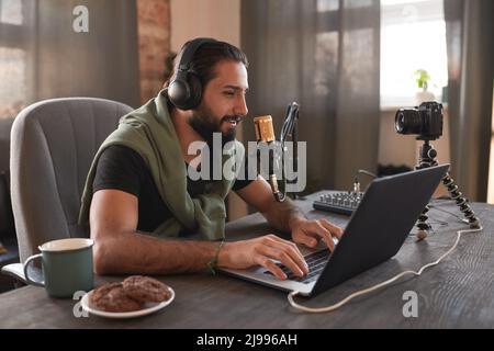 Horizontal medium portrait of handsome bearded young Middle Eastern man sitting alone in loft room creating content for blog Stock Photo