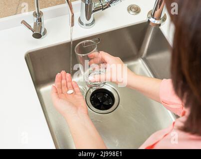 a woman takes a pill and drinks it with water Stock Photo