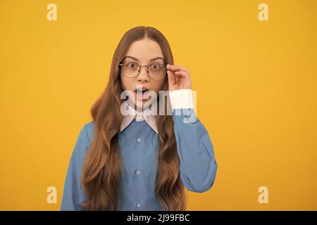 Surprised teenage girl fix eyeglasses yellow background, surprise Stock Photo