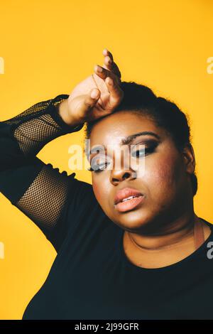 closeup portrait of a thoughtful black woman with crossed arms on yellow background studio Stock Photo