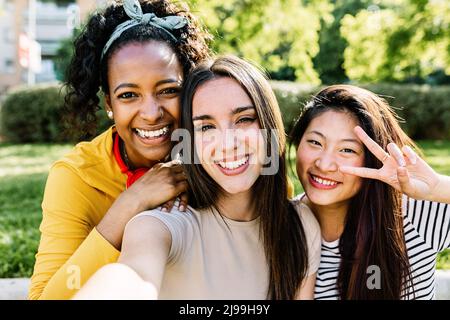 Smiling diverse young female friends taking selfie portrait by mobile phone Stock Photo