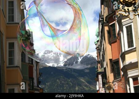 A large soap bubble with rainbow colors floats in the sky, framed by old buildings in Innsbruck. Stock Photo