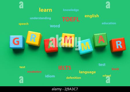 Text GRAMMAR made of wooden cubes and different words on green background. Concept of studying English Stock Photo