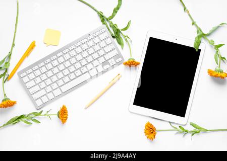 Tablet with computer keyboard, pens, sticky note and flowers on white background Stock Photo