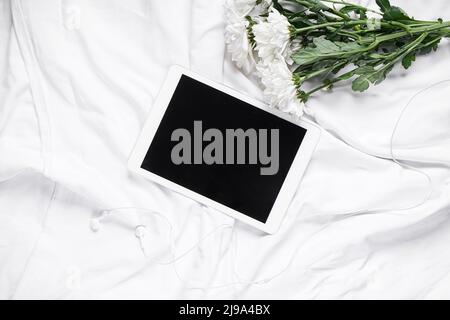 Tablet computer with earphones and flowers on white fabric background Stock Photo