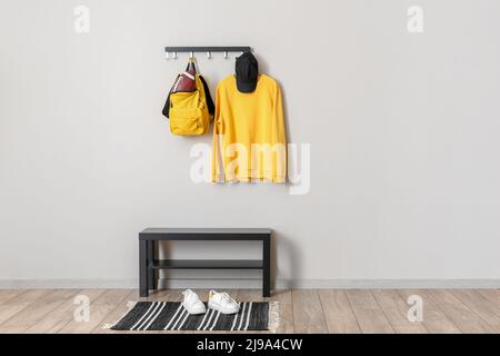 Rugby ball in backpack and clothes on hanger and shoes near light wall Stock Photo