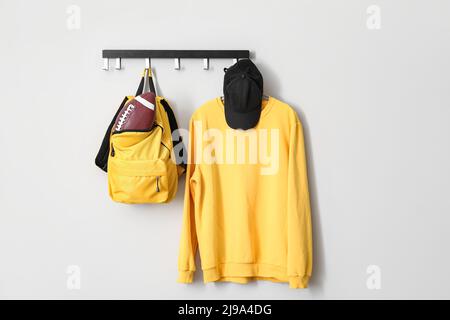 Rugby ball in backpack and clothes hanging on light wall Stock Photo