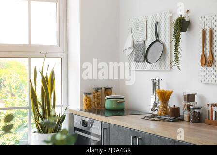 Stylish counters with utensils and pegboards on light wall in kitchen Stock Photo