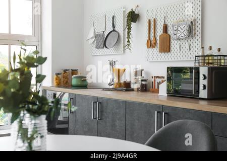 Stylish counters with utensils and pegboards on light wall in kitchen Stock Photo
