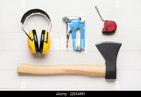 Protective yellow headphones, building stapler, ruler and ax on white wooden background Stock Photo
