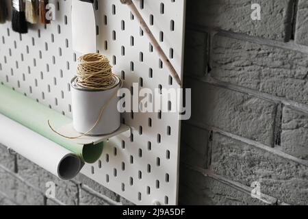 Pegboard with tin can of paint and twine rope on grey brick wall Stock Photo