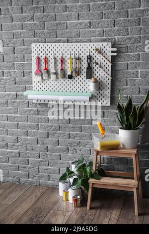 Stepladder stool with houseplant and pegboard with decorator's tools on grey brick wall in room interior Stock Photo
