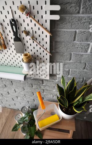 Stepladder stool with paint roller, houseplant and pegboard with decorator's tools on grey brick wall Stock Photo