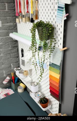 Pegboard with houseplants and tin cans of paint, closeup Stock Photo
