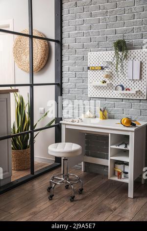 Interior of room with stylish workplace and pegboard on grey brick wall Stock Photo
