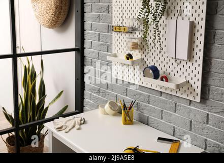Desk and pegboard with tools on grey brick wall Stock Photo