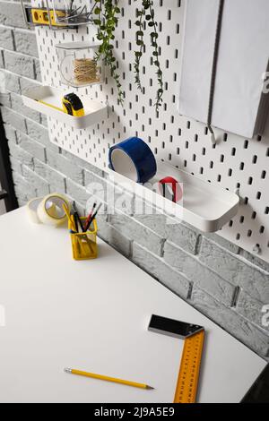 Pegboard with insulation tape and different tools on grey brick wall Stock Photo
