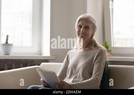 Happy lady holding tablet computer, sitting on comfortable sofa Stock Photo