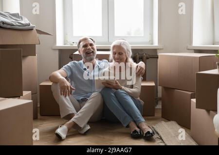 Happy elder 60s married couple using tablet at moving boxes Stock Photo