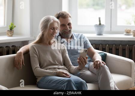 Happy elder married couple using mobile phone at home Stock Photo