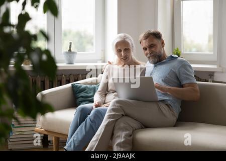 Happy focused elder 60s couple sitting on couch at home Stock Photo