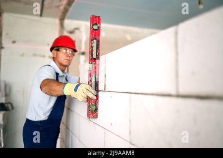 Bricklayer using spirit bubble and laser level to precise check concrete blocks on wall. Contractor uses tools for brickwork. Worker constructs a wall Stock Photo