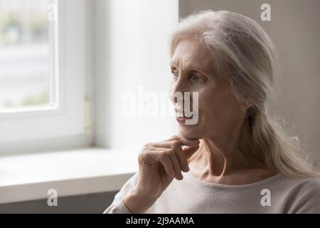 Happy thoughtful senior 70s lady looking away, touching chin Stock Photo