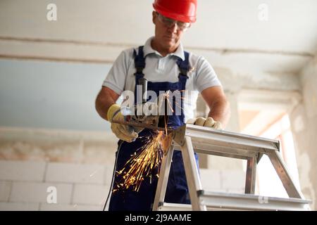 Professional construction worker hands in work gloves using angle grinder to cut metal rod at building site. Close up shot of contractor cutting iron Stock Photo