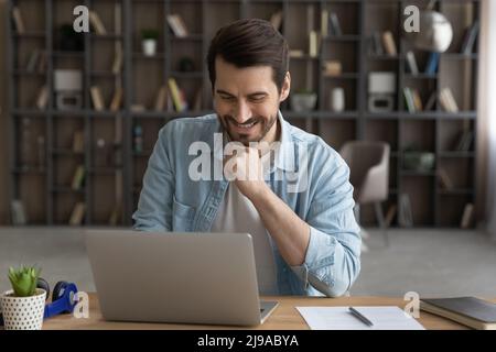 Happy millennial businessman corresponding online using laptop at home office Stock Photo