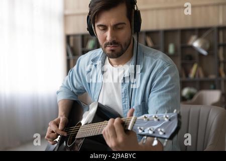 Focused young guy in headset play acoustic guitar at home Stock Photo