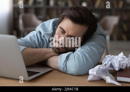 Tired male writer lie on desk sleep among crumpled papers Stock Photo