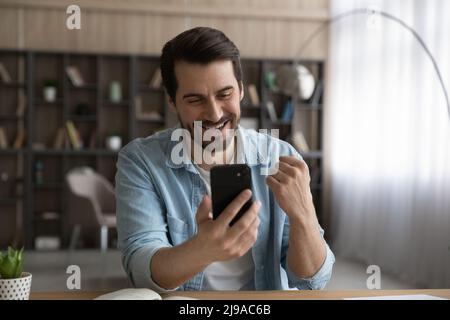 Joyful young bearded male enjoy winning message on cell screen Stock Photo