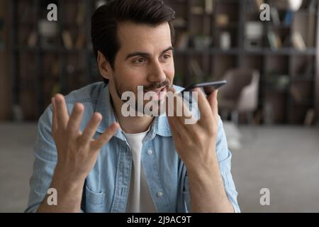 Happy millennial male hold mobile phone using digital voice recorder Stock Photo
