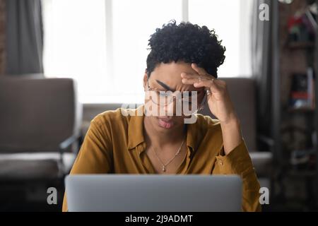 Frowning African woman sit with laptop looks tired, feeling badly Stock Photo