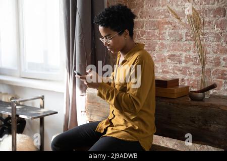 Serious African curly haired woman sit indoors with smartphone Stock Photo