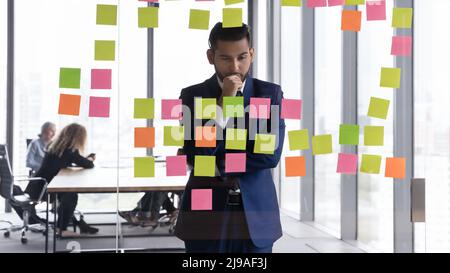 Indian businessman staring at attached adhesive sticky notes with tasks Stock Photo