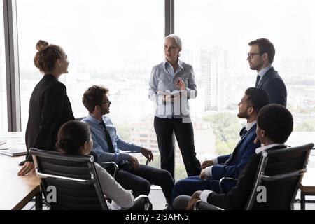 Older company boss leads briefing with young staff in office Stock Photo