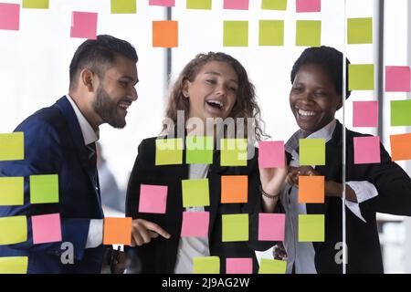 Overjoyed diverse colleagues work together review tasks written on notes Stock Photo