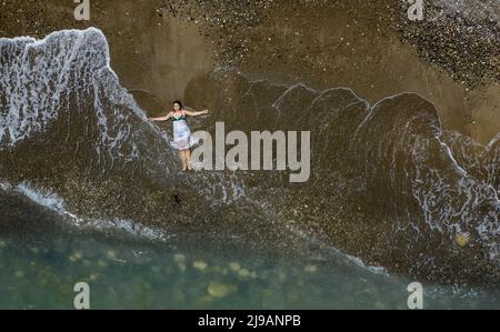 Woman sunbathing on a sandy beach with breaking waves on the shore. Stock Photo