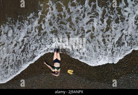 Woman sunbathing on a sandy beach with waves crashing on the shore. Stock Photo