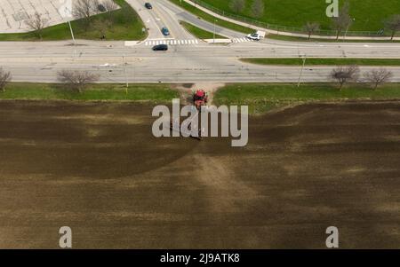 An aerial view above a field as a large, red tractor is seen leaving a field at the beginning of the farming season. Stock Photo