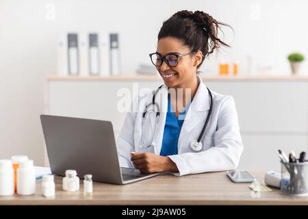 Portrait of smiling doctor looking at screen sitting at desk Stock Photo