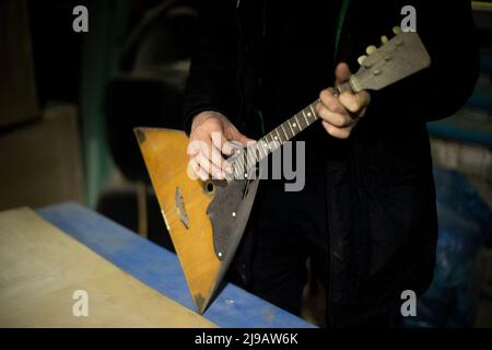 Russian musical instrument balalaika. Three-string acoustic instrument. Guy holds balalaika in his hands. Stock Photo