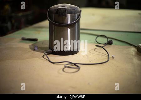 Old thermos. Electrical equipment on table. Boiler for warming water. Repair of electric kettle. Stock Photo