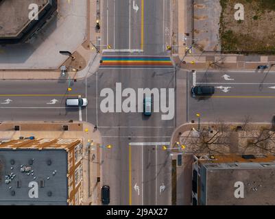 The Rainbow flag (LGBT+) aka the Pride flag is seen painted on a road, seen from above an intersection during the day; from a high aerial perspective. Stock Photo