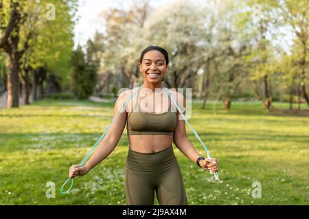 Happy young black woman in sportswear posing with jumping rope at city park