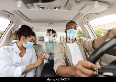 Black Family Of Three Using Sanitizer In Car, Disinfecting Hands Stock Photo