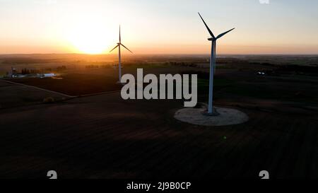 Two wind turbines are pictured at sunset, as the rural landscape is captured as the dusk sun shines bright. Stock Photo