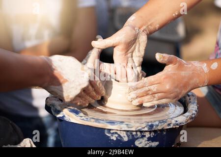 Potter's hands guiding child's hands to help him to work with the pottery wheel Stock Photo