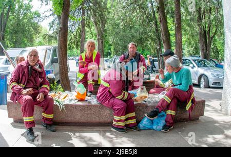 15 May 2022 Bucharest Romania workers sitting together in the square on a stone dressed in red during a lunch break and trees can be seen in the backg Stock Photo